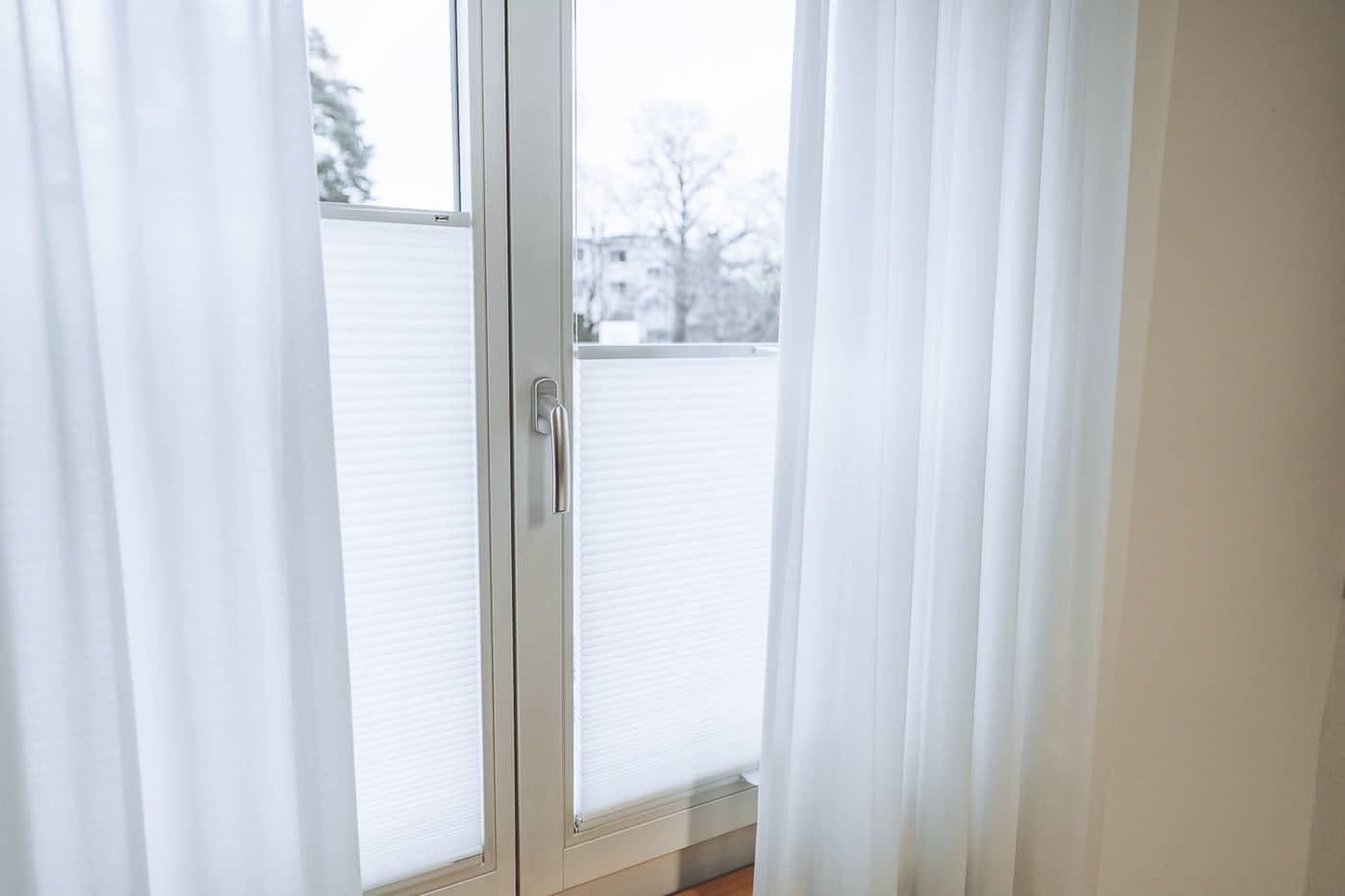 Hinter den Tagesvorh&auml;ngen am Fenster h&auml;ngen zus&auml;tzliche Plissees, die verhindern, dass die hineinfallende Sonne blendet